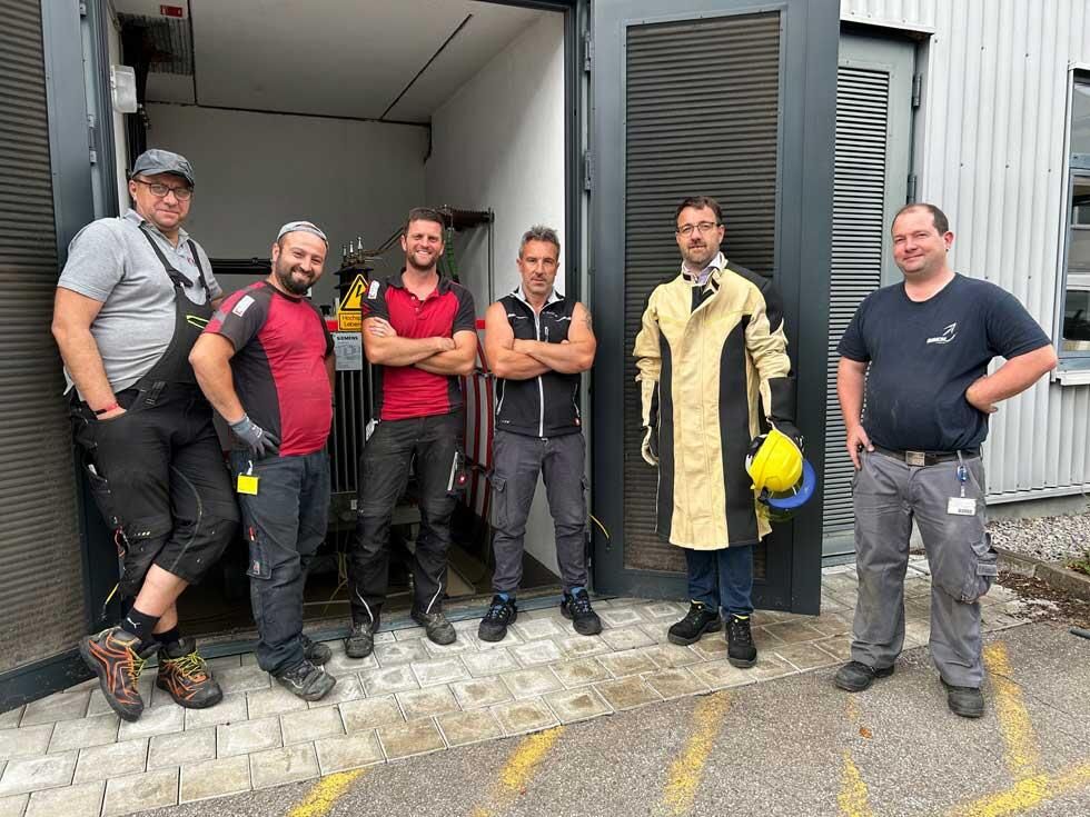 Sechs Installationsmonteure stehen vor einem Gebäude mit geöffneten Toren